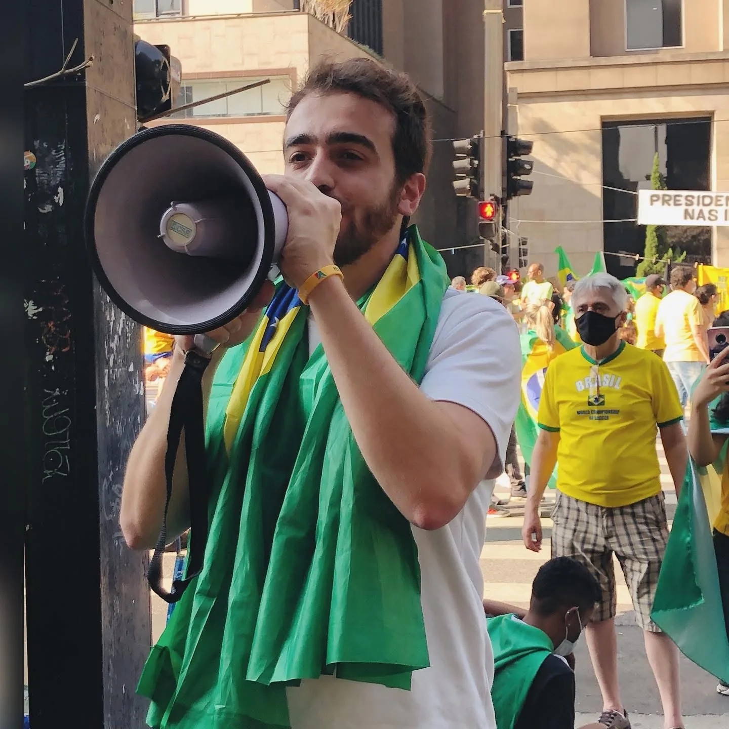 Henrique Krigner fala ao megafone, envolto na bandeira do Brasil, em manifestação na Avenida Paulista